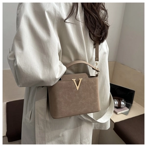 Détail du sac en cuir mat marun avec fermoir doré en V porté sur un long trench-coat chic