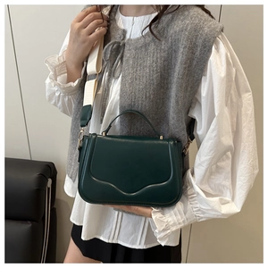 Close-up of dark green crossbody bag featuring wavy flap and stylish cream strap detail