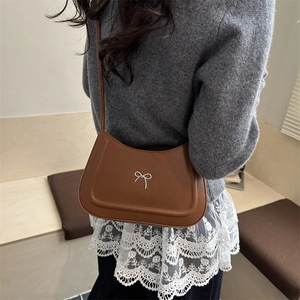 Borsa a spalla a mezzaluna marrone con fiocco argento indossata da modella su maglione grigio