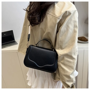 Detail view of black leather crossbody bag with metal handle and contrast strap