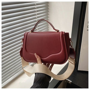 Detail of burgundy leather crossbody bag with wide cream fabric strap and gold hardware