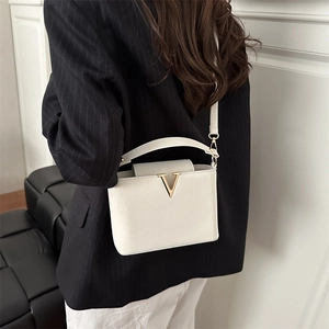 Sac bandoulière carré beige minimaliste avec ornement V doré porté par le mannequin