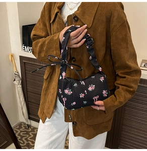 Floral black shoulder bag with pink bow accents and ruched handle detail in casual setting