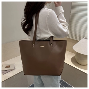 Detail of a minimalist dark brown leather tote bag with gold hardware worn on shoulder
