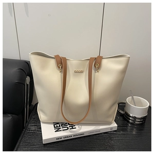 Detail of minimalist cream tote bag with brown straps and gold hardware on books
