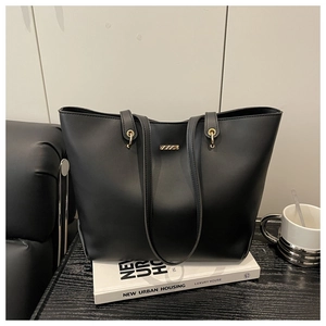 Macro detail of black matte leather tote bag with gold hardware on a modern workspace