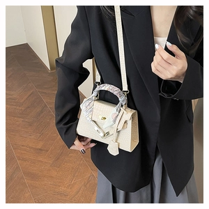 Detail of cream beige crocodile pattern mini bag with decorative silk scarf on handle