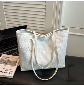 Close-up of white embossed leather tote bag with laptop and book in office setting