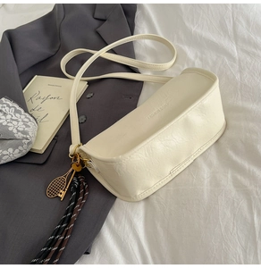 Detail view of cream white shoulder bag with golden tennis racket charm and braided rope