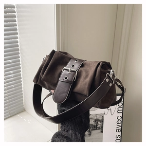 Details einer dunkelbraunen Wildleder-Schultertasche mit breitem Ziergurt und Metallschnalle