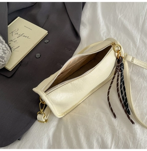 Detail of cream barrel crossbody bag showing zip closure, inner lining, and woven tassel