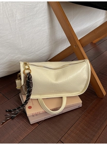 Detail of creamy textured leather handbag with gold zipper and tennis racket charm