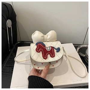 Detail van crème mini-crossbodytas met grote strik en pony-borduurwerk op een boek