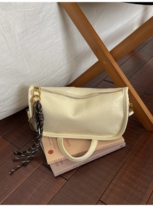 Detail of cream barrel bag with pleated leather, tennis racket charm and long tassel