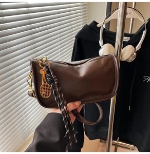 Detail of dark brown vintage leather bag featuring a gold tennis racket charm and tassel