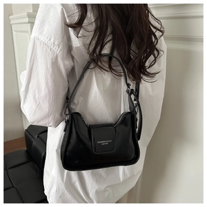 Détail d'un sac sous les bras noir brillant avec texte blanc porté sur une chemise blanche