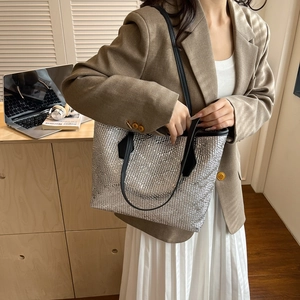 Silver metallic woven tote bag with black handles in a casual lifestyle setting