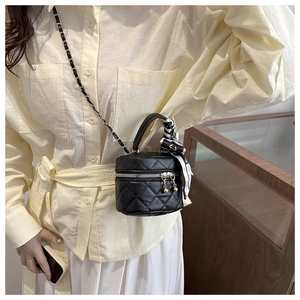 Detail of black quilted mini cylinder bag featuring silk scarf handle and chain strap