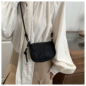 Detail of a black crossbody saddle bag with knotted strap and silver M-letter hardware