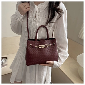 Detail of burgundy woven handbag with golden metal knot buckle and dual top handles