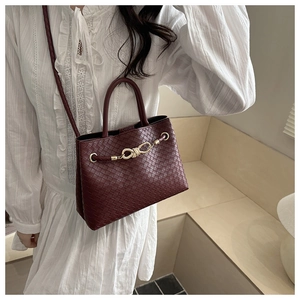 Detail of burgundy woven crossbody bag with gold bow clasp on white ruffled shirt