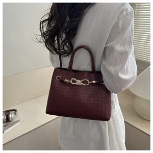 Detail of dark red woven handbag featuring a gold knot-shaped metal clasp shown on shoulder