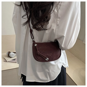 Detail view of burgundy saddle bag featuring knotted strap and metal letter decoration