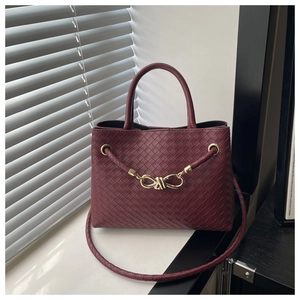Detail of burgundy woven leather handbag with gold bow clasp and stylish braided strap