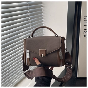 Close-up of brown cross-grain leather bag with silver buckle and wide woven strap