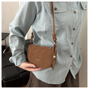 Close-up of a brown matte saddle bag with metal M-pendant and elegant silver zipper