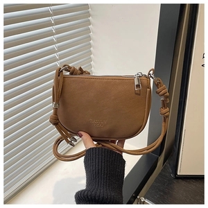Close-up of retro brown saddle bag featuring knot detail strap and silver zipper closure