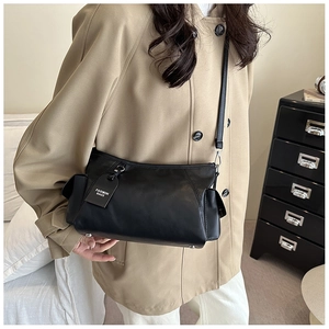 Detail view of the black matte crossbody bag with side accordion folds and brand tag