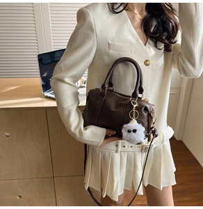 Brown vintage boston bag with plush pom-pom charm shown in a professional office setting