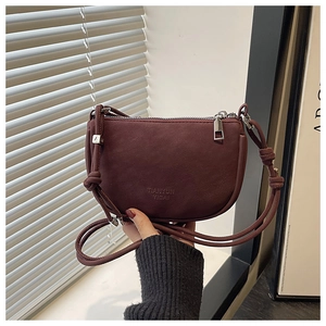 Detail of burgundy leather half-moon crossbody bag with knot strap and metal pendant