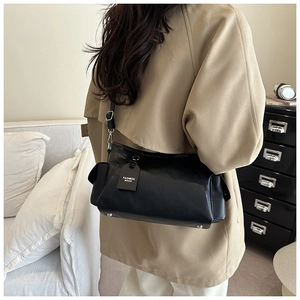 Rear view of minimalist black leather crossbody bag worn over a beige trench coat