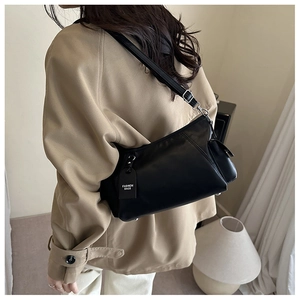 Detail of black leather shoulder bag with FASHION BAGS tag on a model in khaki coat