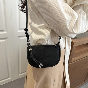 Minimalist black saddle crossbody bag with silver metal charm on a light-colored outfit