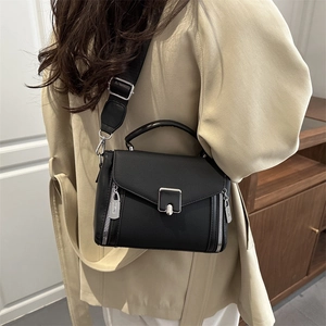 Black structured leather crossbody bag with silver hardware on a beige trench coat