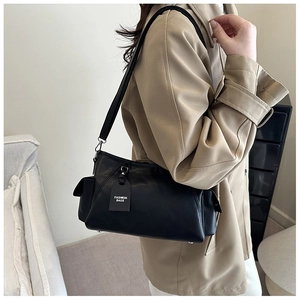 Detail of minimalist black leather tote bag featuring fashion tag and adjustable strap