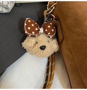 Detail eines Plüschbär-Anhängers mit gepunkteter Schleife an einer braunen Ledertasche