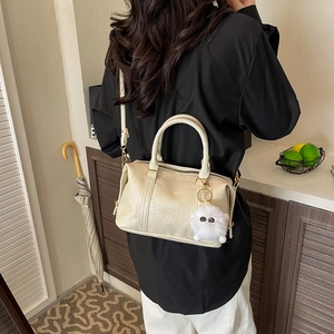 Creamy white Boston bag with embossed text and plush charm shown in a cozy home setting