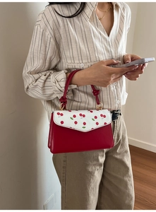Detail of red cherry print flap handbag with knotted soft handle carried by a model