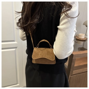 Petit sac à bandoulière vintage marron porté par un mannequin dans un décor épuré
