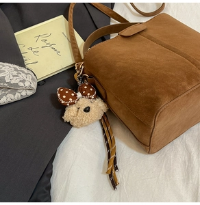 Detailaufnahme der braunen Wildledertasche mit süßem Plüschwelpen-Anhänger und Gurt