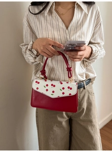 Detail of red leather handbag with cherry pattern flap and elegant gold hardware