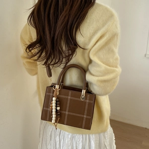 Vintage brown leather handbag with white stitching and bead tassel on a model
