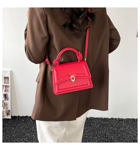 Detail of red leather crossbody bag with knot handle and gold clasp on a model
