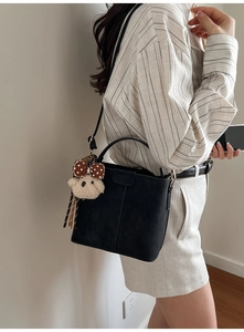 Detail der schwarzen Wildleder-Eimertasche mit Teddybär-Anhänger und Metallschließe