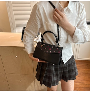 Detail of black PU crossbody bag with pink floral and bow patterns in a lifestyle setting