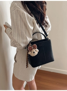 Detail der schwarzen matten Leder-Eimertasche mit Tragegriff und süßem Teddybär-Anhänger